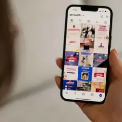Dłoń trzyma smartfon z widokiem profilu Instagram z różnymi postami.