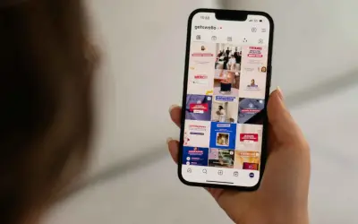 Dłoń trzyma smartfon z widokiem profilu Instagram z różnymi postami.