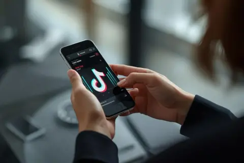 Dłonie trzymające smartfon z otwartą aplikacją TikTok i widocznymi statystykami.
