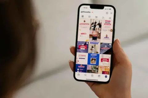 Dłoń trzyma smartfon z widokiem profilu Instagram z różnymi postami.