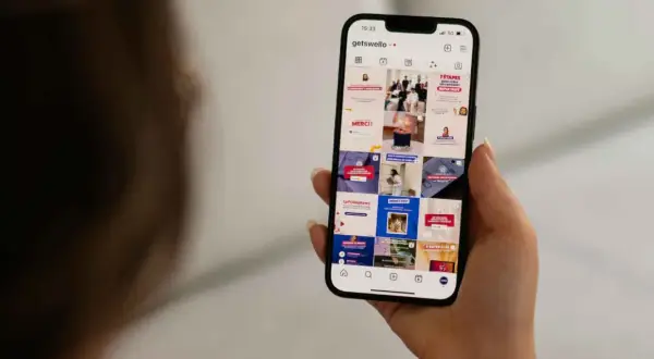 Dłoń trzyma smartfon z widokiem profilu Instagram z różnymi postami.